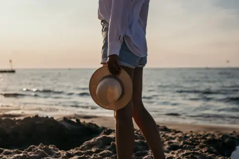 Sonnenuntergang am Kolberg Strand. Eine Frau hält einen Strohhut, während sie am Wasser entlang spaziert.