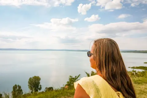 Kobieta w żółtej bluzce patrzy na rozległe jezioro, zastanawiając się, gdzie nad Balaton.