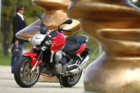 Czerwona Aprilia Mana 850 z chromowanym wydechem, obok mężczyzny w garniturze.