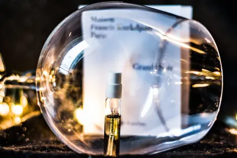 Mała próbka perfum Grand Soir Maison Francis Kurkdjian w szklanej kuli, otoczona ciepłym światłem.