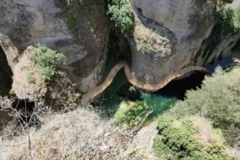 Un puente serpentea sobre el agua verde en el tajo de Ronda, rodeado de rocas y vegetación.