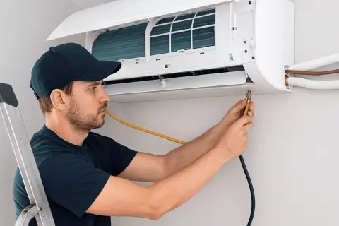 Técnico instalando aire acondicionado, conectando manguera amarilla a la unidad interior.