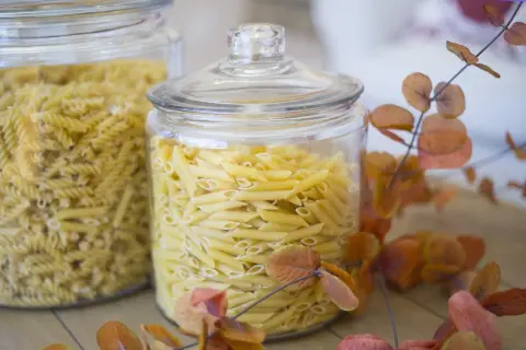 Zwei Glasbehälter voller Nudeln, Penne und Spiralen. Die Frage "wie lange sind nudeln haltbar" wird durch die frische Optik der ungekochten Pasta beantwortet.