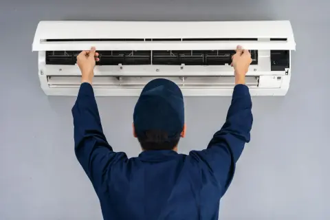 Tecnico con cappellino blu apre il pannello di un condizionatore per manutenzione.