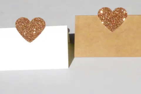 Segnaposto nozze d'oro fai da te: due cartoncini, uno bianco e uno kraft, decorati con cuori glitterati color oro.