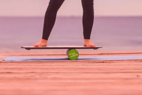 Füße balancieren auf einem Wackelbrett über einer Rolle.