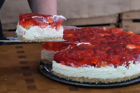 Krojony tort z galaretką truskawkową i bitą śmietaną na spodzie z ciastek.