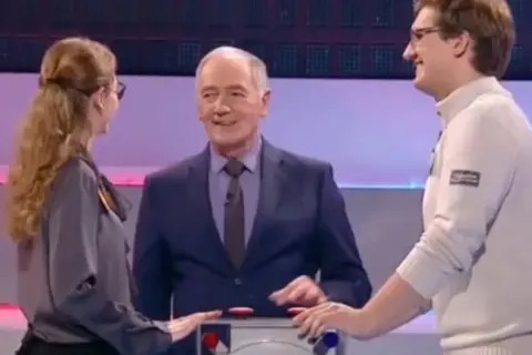 Trzy osoby na planie teleturnieju Familiada: prowadzący i dwoje uczestników.