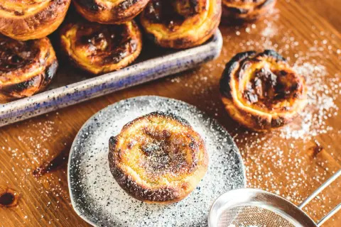 Köstliche, karamellisierte Pastéis de Nata, bestäubt mit Puderzucker, warten auf dem Holztisch.