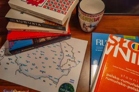 Książki i kubek z motywami Rumunii, w tym słownik polsko-rumuński, zachęcają do nauki języka rumuńskiego.
