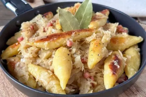 Nudeln mit Sauerkraut und Speck in einer Pfanne, garniert mit Lorbeerblättern.