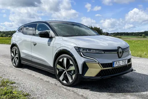 En vit Renault Megane E-Tech står parkerad på en grusväg med en gul och grön fält i bakgrunden. En del av en testkörning.