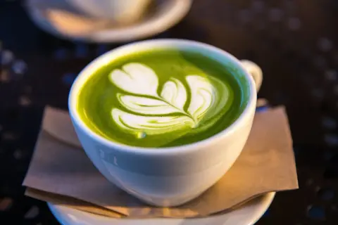 Un délicieux matcha lait d'avoine avec un art latte en forme de feuille, servi dans une tasse blanche sur une soucoupe.