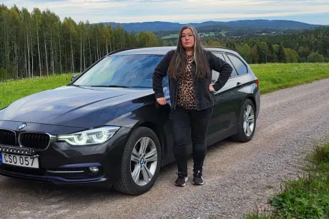 Kvinna vid en svart BMW kombi i svensk landsbygd. Kanske ett bmw b47 problem som gör att hon stannat här.