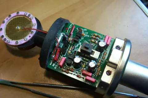 Elementy budowy mikrofonu: płytka drukowana z elementami elektronicznymi, kapsuła z membraną i pęseta.
