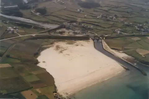 Vista aérea de una playa pampillosa con arena clara, bordeada por un río y campos verdes.