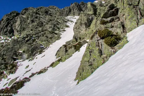 Canal de nieve y roca en la ladera de la Maliciosa, con vegetación escasa y un cielo azul intenso.