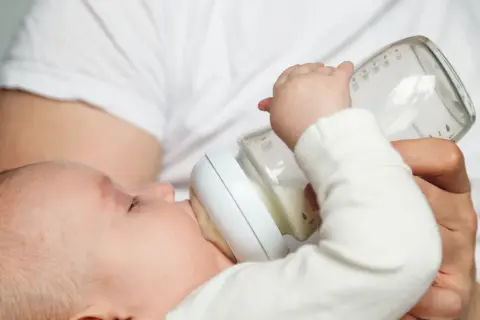 Malutki głodomór pije mleko modyfikowane z butelki. Dziecko z zapałem pochłania każdy łyk, bo przecież noworodek ciągle głodny na mleku modyfikowanym potrzebuje siły.