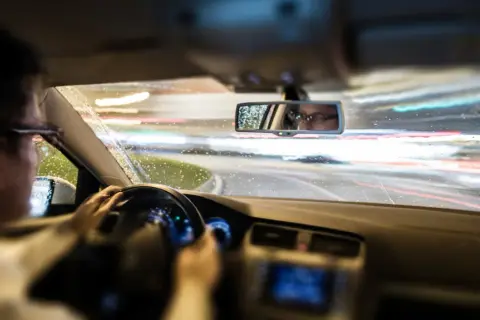 Conductor con gafas al volante de noche, con lluvia y luces de coches borrosas. El ASR de un coche ayuda a mantener la tracción en estas condiciones.