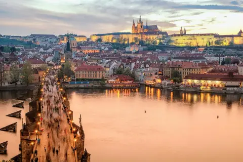 En folktät Karlsbro i Prag vid skymningen, med upplysta byggnader och Pragborgen i bakgrunden. En klassisk vy att se i Prag.