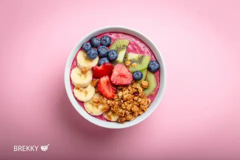 Eine bunte Acai Bowl mit Bananen, Erdbeeren, Blaubeeren und Kiwi, garniert mit Granola.