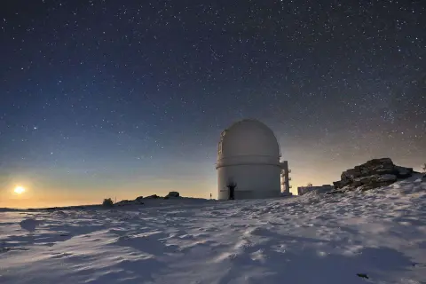Observatorio en el calar alto bajo un cielo estrellado. La luna ilumina un paisaje nevado y rocoso.