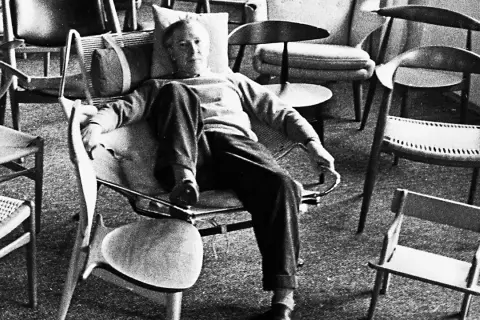 Hans J Wegner, a master of Danish design, relaxes amidst his iconic chairs, surrounded by his timeless creations.