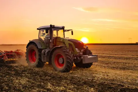 Un tracteur, c'est ce puissant engin vert et rouge qui travaille la terre au coucher du soleil, préparant le champ pour les futures récoltes.