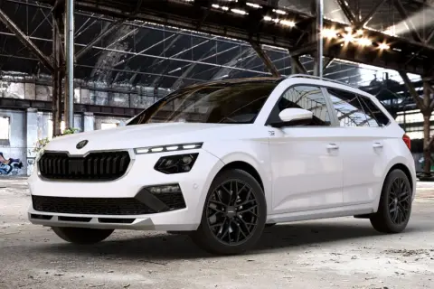Biała Skoda Kamiq Monte Carlo z czarnymi felgami i detalami, zaparkowana w opuszczonej hali przemysłowej z graffiti.