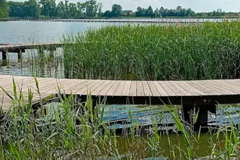 Spokojny wędkarz na drewnianej kładce nad jeziorem słupeckim, otoczony szuwarami.
