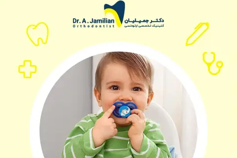 A baby with a pacifier, or binky, in their mouth. The pacifier has a blue elephant design.