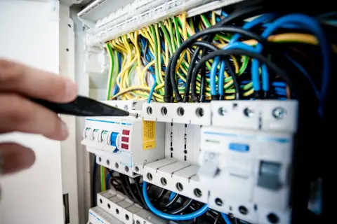 Main électrique avec fils colorés. Un tournevis ajuste un disjoncteur, peut-être un délesteur électrique, dans un tableau.
