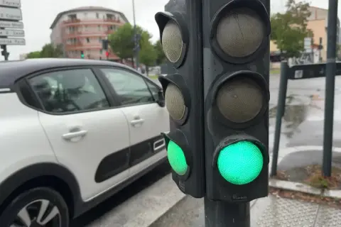 Un feu de circulation vert est allumé, indiquant que la circulation peut passer. Le gyrophare vert signification est la permission de continuer. Une voiture blanche est garée à proximité.
