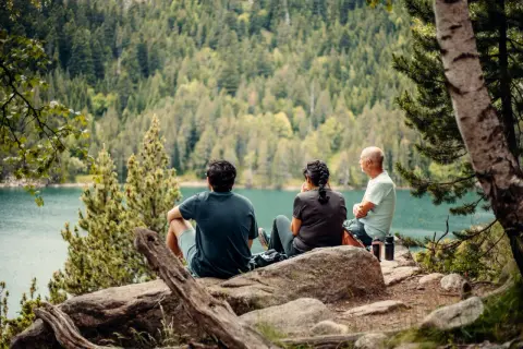 Tres personas disfrutan de las vistas del lago y el bosque, un descanso perfecto en las rutas Vall de Boí.