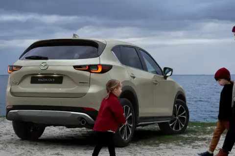 Rodzina przy nowej Mazdzie CX-5 na tle morza. Dzieci i matka spacerują brzegiem.