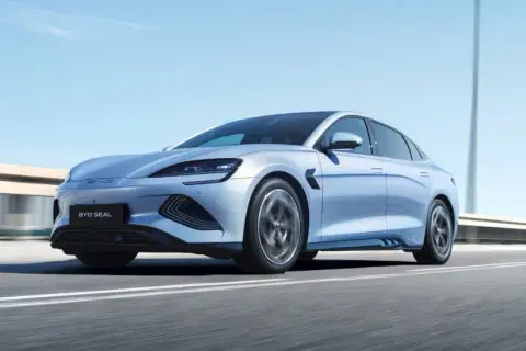 Un elegante veicolo elettrico BYD Seal sfreccia su un'autostrada soleggiata, con il cielo azzurro e le luci stradali sfocate sullo sfondo.