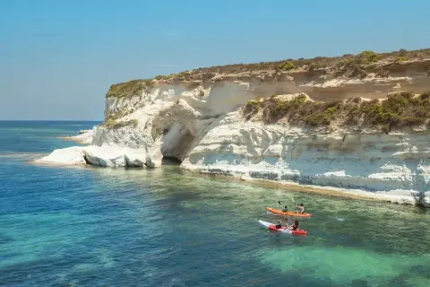 Malta, październik: kajaki w turkusowej wodzie przy klifie z jaskinią. Idealna pogoda na wodne przygody.