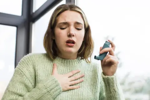Kobieta z astmą używa inhalatora, trzymając rękę na klatce piersiowej.