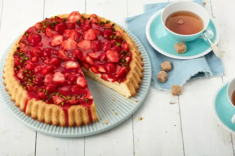 Ein schneller Erdbeerkuchen mit Paradiescreme, belegt mit frischen Erdbeeren und Pistazien. Dazu eine Tasse Tee.