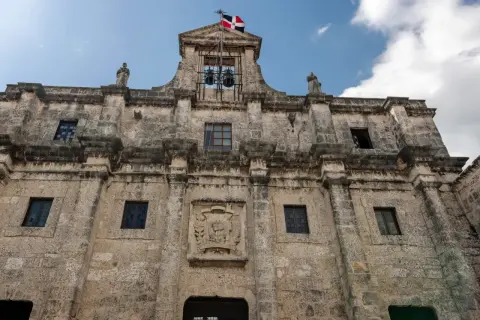 Kamienna fasada Alcázaru de Colón w Santo Domingo, z dzwonami i flagą Dominikany.