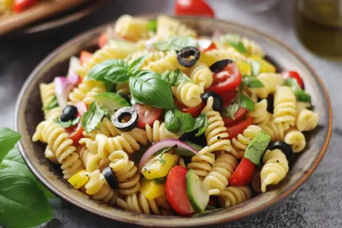 Un piatto invitante di pasta fredda con pomodorini, olive nere, cetrioli, cipolla rossa e basilico fresco.