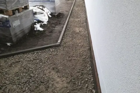 Wykonano opaskę wokół domu z żwiru, obok składowane są materiały budowlane.