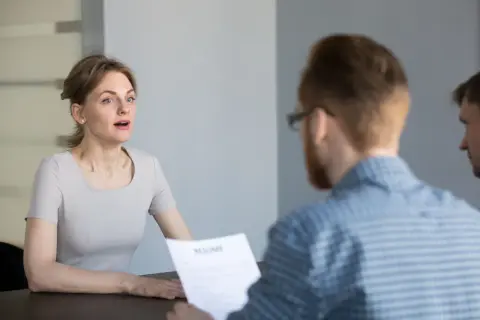 Kobieta podczas rozmowy kwalifikacyjnej, patrząca na rozmówcę trzymającego CV.