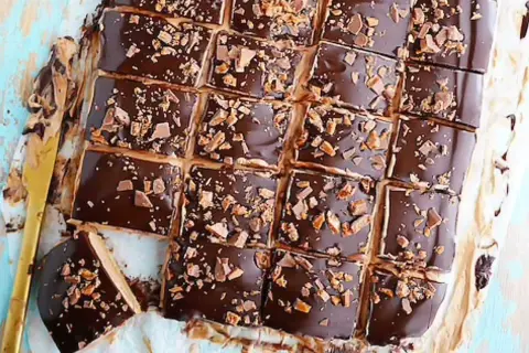 Biskvier i långpanna från Lindas bakskola, täckta med choklad och strössel. En gyllene kniv ligger bredvid.