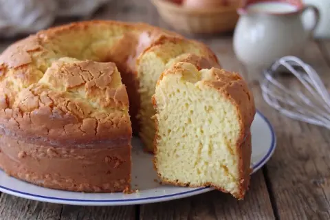 Il ciambellone della nonna, soffice e dorato, pronto per essere gustato. Sullo sfondo, uova e latte, ingredienti essenziali.