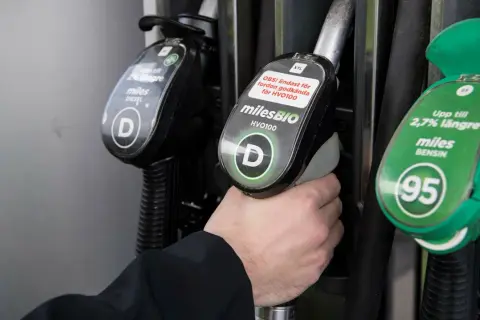 Hand håller dieselslang, funderar på dieseltillsats bra eller dåligt. Bredvid finns bensinslang.