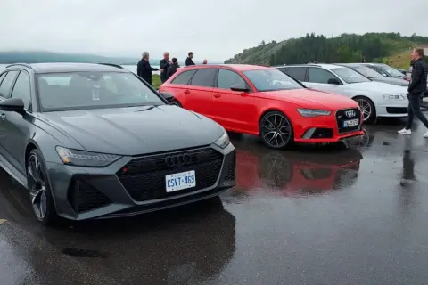 Szare i czerwone Audi RS6 C8 stoją obok siebie na mokrym parkingu.