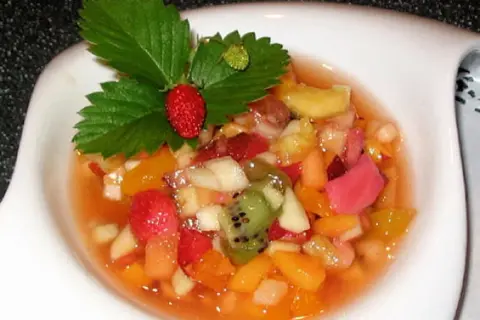 Salade de fruits maison colorée, garnie d'une fraise et de feuilles de fraisier.