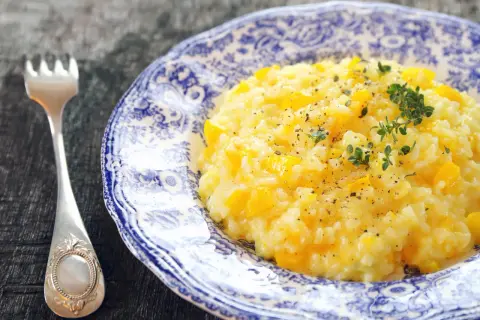Pyszny, kremowy ryż do risotto z kawałkami dyni, posypany świeżym tymiankiem i pieprzem. Obok leży elegancki widelec.