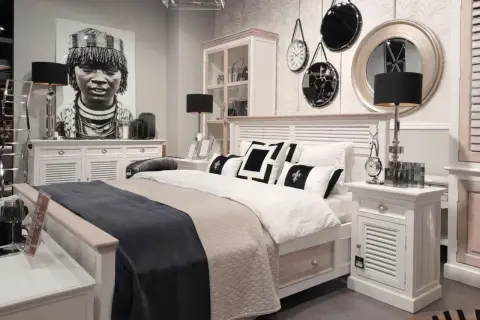 Sypialnia boho loft z łóżkiem, czarnymi lampami i portretem kobiety. Dekoracje ścienne dodają charakteru.